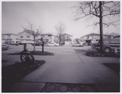 Black and white pinhole photograph of a suburban street scene
